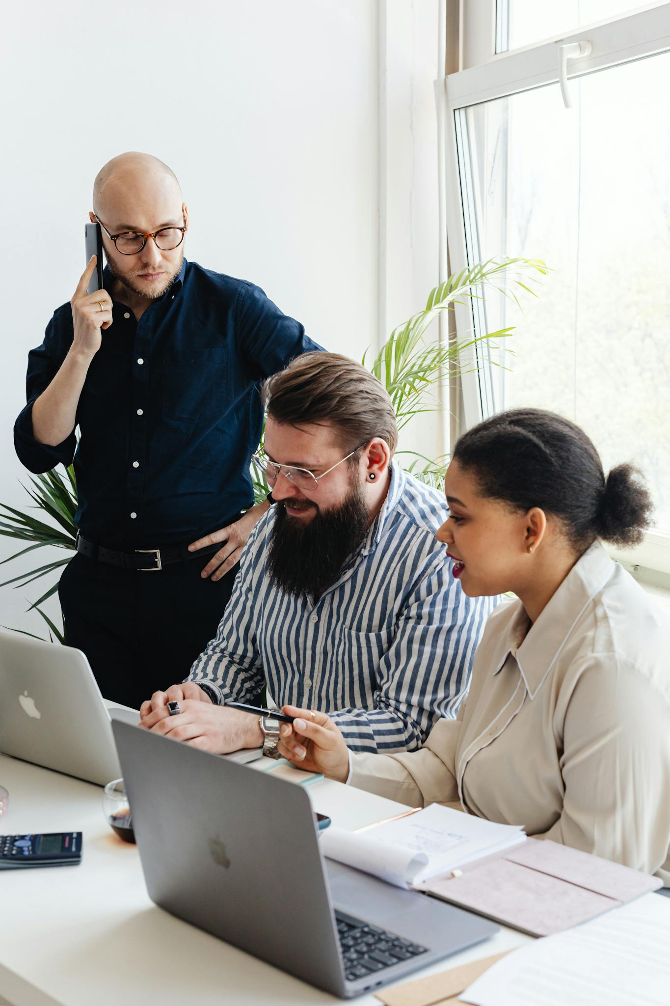 A diverse group of professionals engaged in a collaborative team meeting at a modern office with laptops and mobile phones.