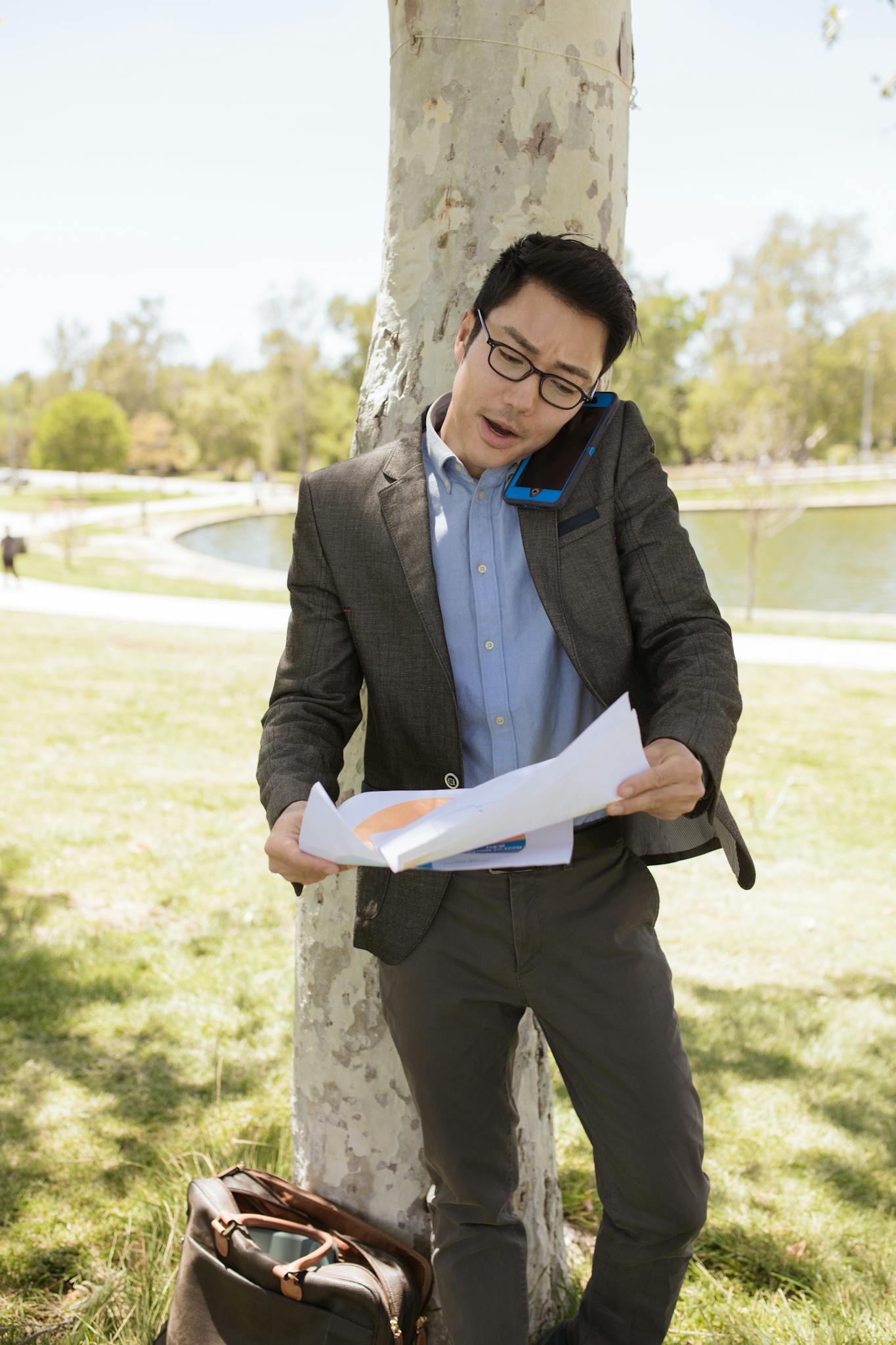 Young businessman in a suit talking on phone and handling documents at a park.